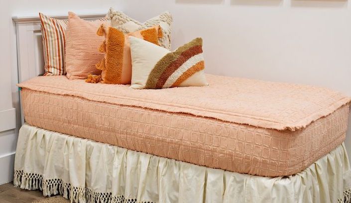 Peach bedding with textured rectangle design with dark cream textured euro, orange, textured pillow with tassels, rainbow lumbar and cream boho bedskirt