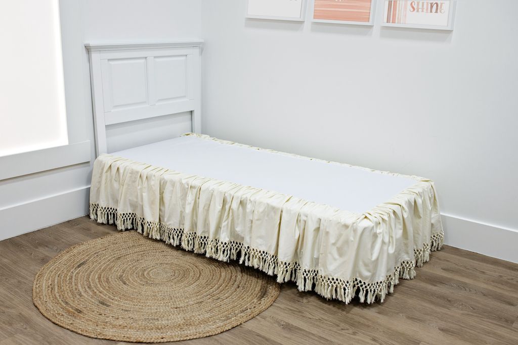 White twin size bed with a cream bed skirt with tassels.
