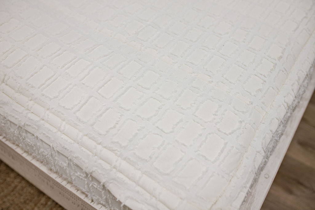 corner of Twin bed with cream bedding with textured rectangle design