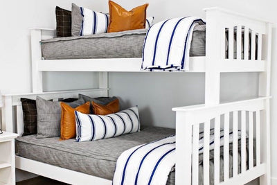 bunk bed with Brown and gray woven textured bedding and with faux leather pillows, white XL lumbar with navy vertical stripes, and white blanket with horizontal navy stripes at the foot of the bed