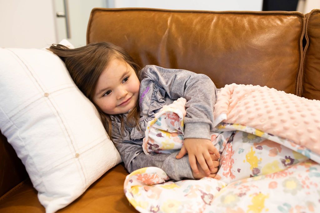 Child laying on couch with white pillow and floral mini blanket
