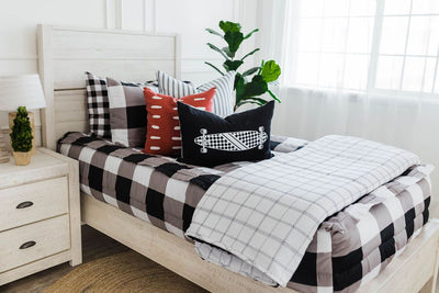 twin bed with Black and white buffalo plaid bedding black and white striped euros, red and white dashed pillow, black lumbar with white longboard print and white and white and black grid blanket