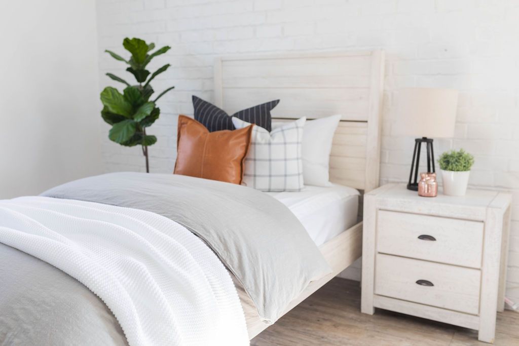 A bed made with white zipper sheets and a slate gray zipper duvet folded half way down the bed and adorned with neutral pillows a white throw blanket.