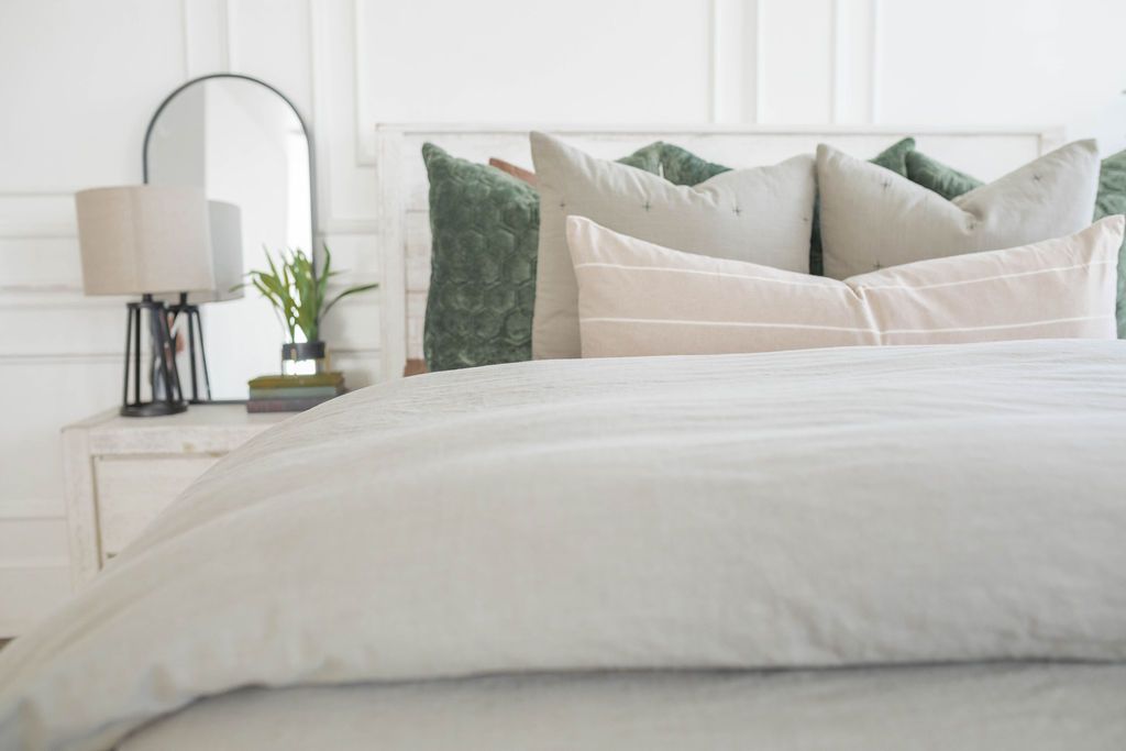 A bed made with a slate gray zipper duvet folded half way down the bed and adorned with neutral and green velvet pillows.