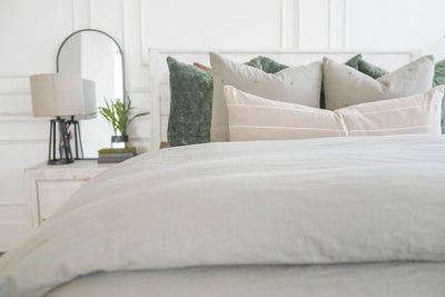 A bed made with a slate gray zipper duvet folded half way down the bed and adorned with neutral and green velvet pillows.