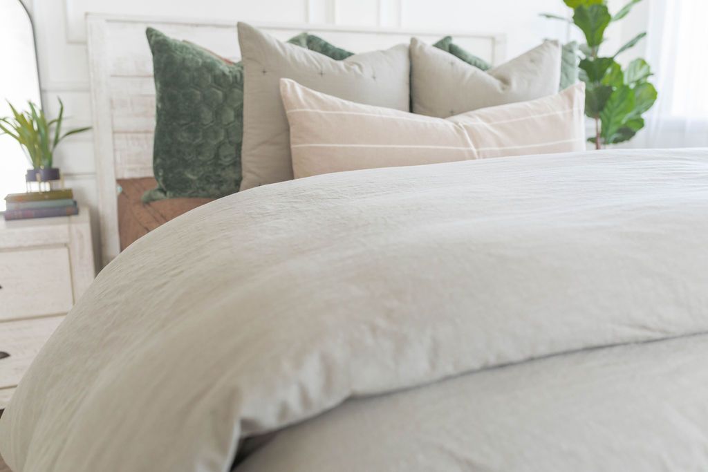 A close up view of a bed made with brown zipper bedding and a slate gray zipper duvet folded half way down the bed and adorned with neutral and green velvet pillows.