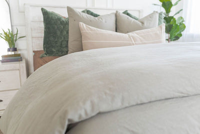 A close up view of a bed made with brown zipper bedding and a slate gray zipper duvet folded half way down the bed and adorned with neutral and green velvet pillows.