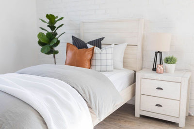 A bed made with white zipper sheets and a slate gray zipper duvet folded half way down the bed and adorned with neutral pillows a white throw blanket.