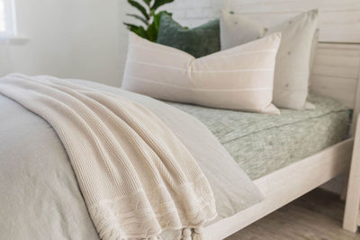 A side view of a bed made with dark emerald green zipper bedding and a slate gray zipper duvet folded half way down the bed and adorned with neutral and green pillows and a throw blanket.