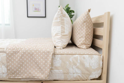 A side shot of a twin bed made with light tan cars kids zipper bedding, the top unzipped and pulled back slightly and two pillows at the head of the bed.