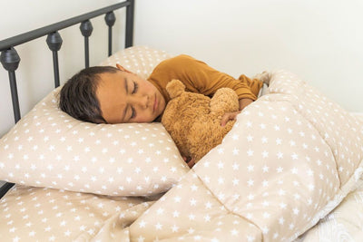 A young boy holding a stuffed animal and sleeping in a bed made with light tan cars kids zipper bedding.