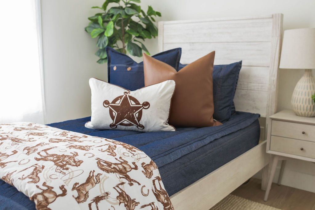 A twin bed made with denim blue zipper bedding and an assortment of neutral western pillows and matching blanket.