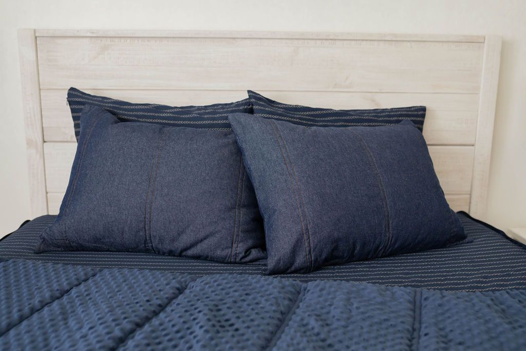 A denim blue zipper bedding made with the matching pillows stacked in the middle of the bed and the comforter pulled back revealing a minky interior.