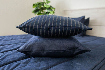 A denim blue zipper bedding made with the matching pillows stacked in the middle of the bed. 