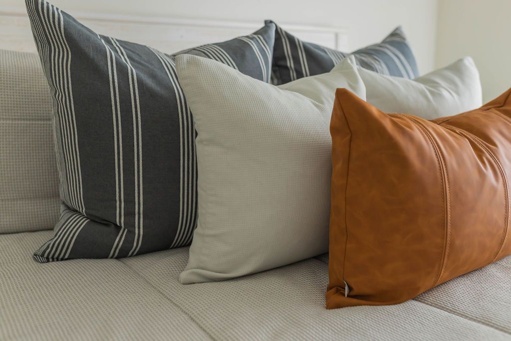 Brown vegan leather lumbar pillow styled on gray zipper bedding with matching pillows