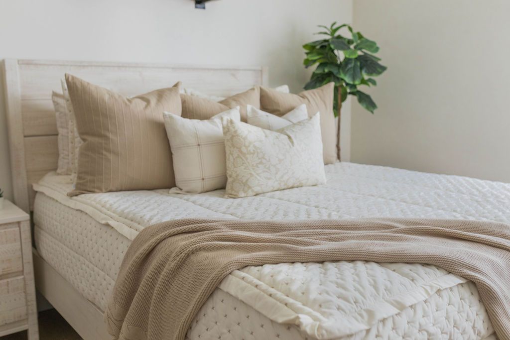 A bed made with cream embroidered zipper bedding, decorated with neutral throw pillows and blanket.