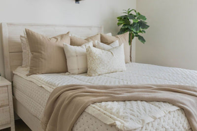A bed made with cream embroidered zipper bedding, decorated with neutral throw pillows and blanket.