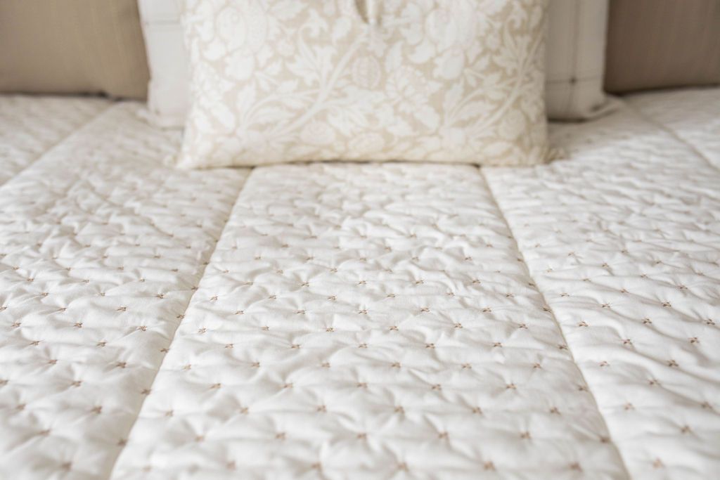 A close up detailed view of a bed made with cream embroidered zipper bedding. 