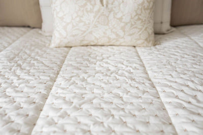 A close up detailed view of a bed made with cream embroidered zipper bedding. 