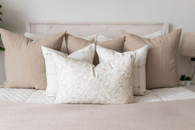 A close up view of a bed made with cream embroidered zipper bedding, decorated with neutral throw pillows and blanket.