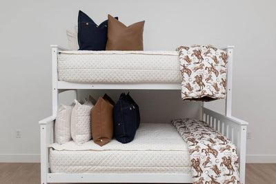 A standard bunk bed with both bunks made with cream embroidered zipper bedding and denim and leather pillows and cowboy western printed blankets.
