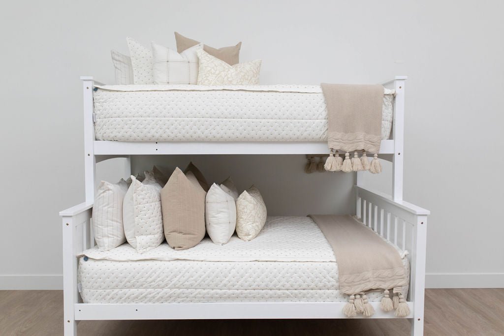 A standard bunk bed with both bunks made with cream embroidered zipper bedding and neutral pattern pillows and blankets.