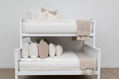 A standard bunk bed with both bunks made with cream embroidered zipper bedding and neutral pattern pillows and blankets.