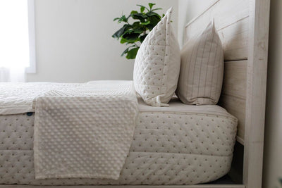 A close up side view of a bed made with cream embroidered zipper bedding with the top unzipped halfway down the bed and the comforter folded down.
