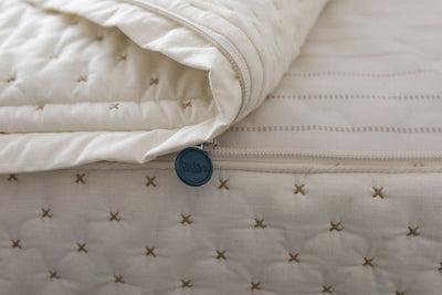 A close up view of a bed made with cream embroidered zipper bedding with the bed slightly unzipped to reveal the minky comforter and the light tan and cream striped pattern bottom cotton lining.