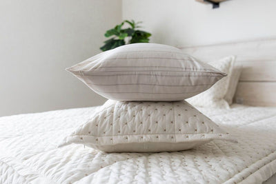A white striped pillowcase and matching sham on a made bed with cream embroidered zipper bedding. 