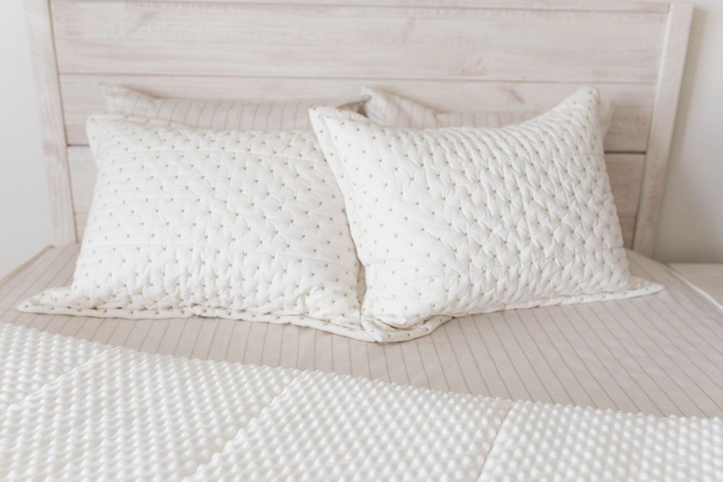A bed made with cream embroidered zipper bedding with the comforter pulled back showing minky interior lining and pillows on top of the bed.
