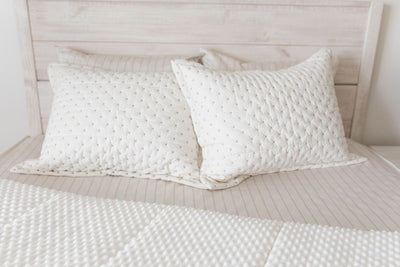 A bed made with cream embroidered zipper bedding with the comforter pulled back showing minky interior lining and pillows on top of the bed.