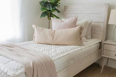 A twin bed made with cream embroidered zipper bedding and adorned with neutral and light pink pillows and a throw tan blanket.