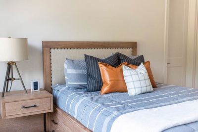queen brown upholstered bed and dresser with deep navy striped euros, faux leather pillows, white and black grid pillow, and white textured blanket with braided tassels