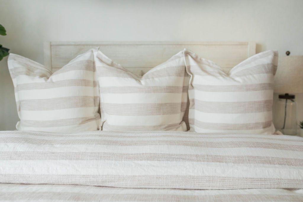 A close up view of a bed made with a cream and tan striped duvet and matching large pillows.