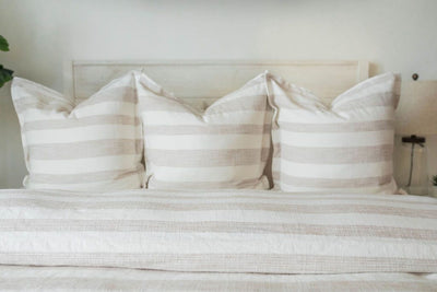 A close up view of a bed made with a cream and tan striped duvet and matching large pillows.