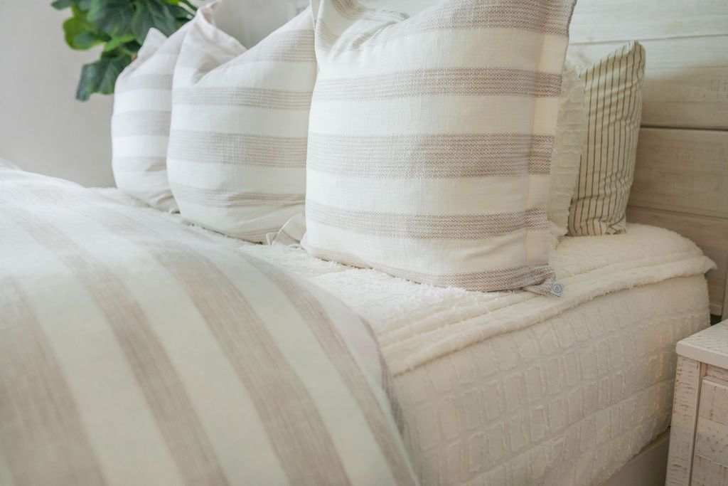 A close up view of a queen bed made with cream textured zipper bedding and a cream and tan striped duvet with matching large pillows.