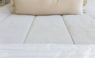 Close up showing texture of light gray zipper bedding with white blanket and cream lumbar pillow.