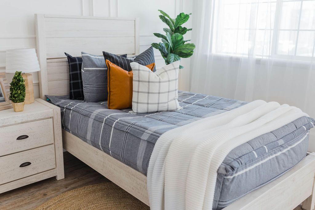 twin bed with Deep navy woven stripe bedding with deep navy striped euros, faux leather pillows, white and black grid pillow, and white textured blanket with braided tassels