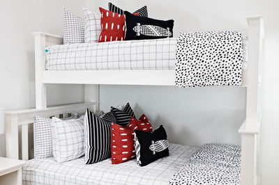 White bunk bed with white and black grid patterned bedding, black and white striped euros, red and white dashed pillow, black lumbar with white longboard print and white and black polka dot blanket
