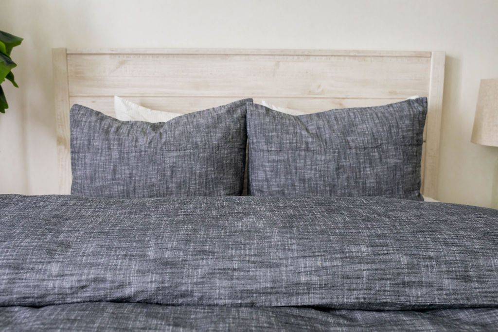 A close up view of a bed made with a dark gray zipper duvet folded down the bed and matching pillows. 