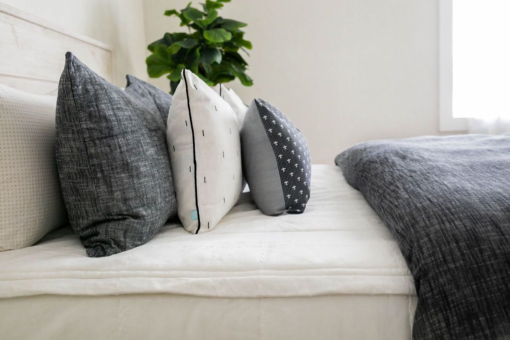 A side view of a bed made with white zipper bedding and a dark gray zipper duvet folded half way down the bed and adorned with neutral black and white pillows.