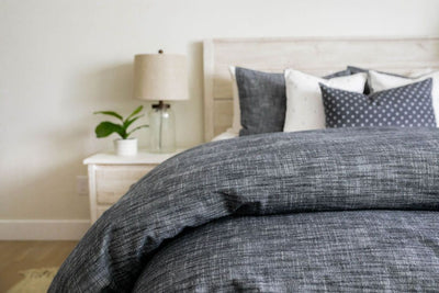 A bed made with a dark gray striped zipper duvet folded half way down the bed and adorned with neutral black and white pillows.