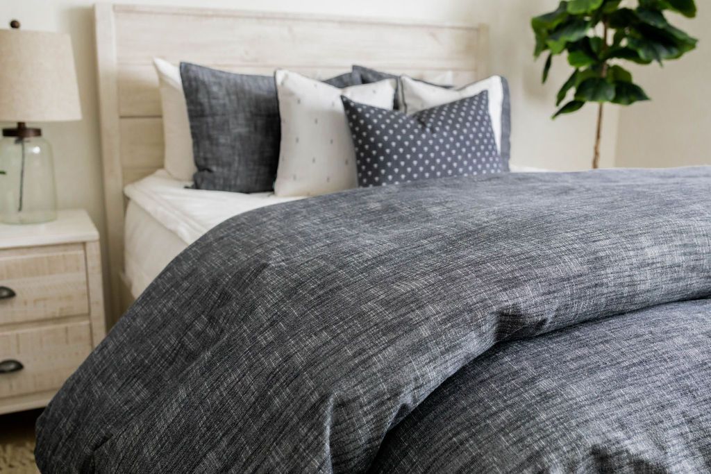 A close up view of a bed made with white zipper bedding and a dark gray zipper duvet folded half way down the bed and adorned with neutral black and white pillows.