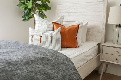 A twin bed made with white zipper bedding and a dark gray zipper duvet folded half way down the bed and adorned with neutral and leather pillows.
