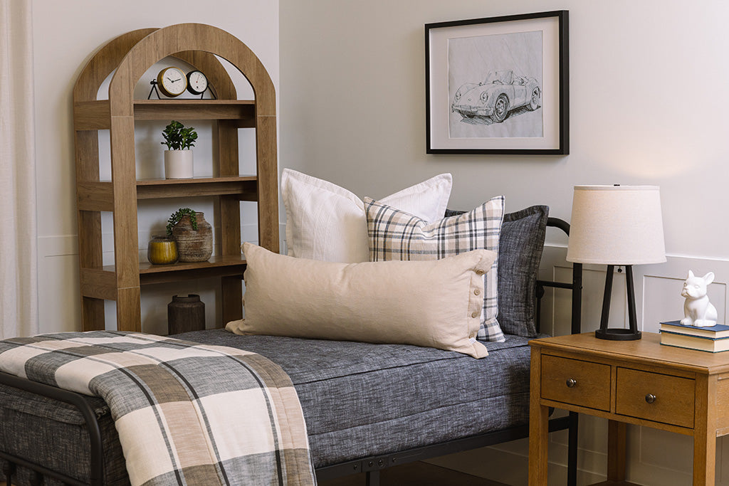 A twin bed made with dark charcoal gray zipper bedding and neutral and white striped pillows and blanket.