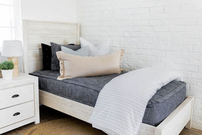 A twin bed made with dark charcoal gray zipper bedding and neutral and white striped pillows and blanket.
