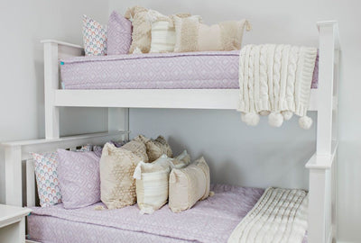 A standard bunk bed with both bunks made with purple textured zipper bedding and neutral cream tasseled pillows and blankets.