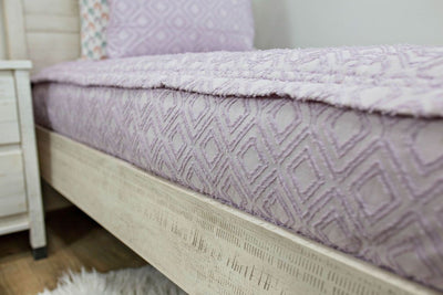A close up side view of a bed made with purple textured zipper bedding.