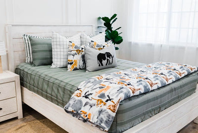 Queen bed with Green striped bedding with white and black grid patterned euro, safari animal print pillow, gray lumbar with embroidered elephant and safari animal print blanket